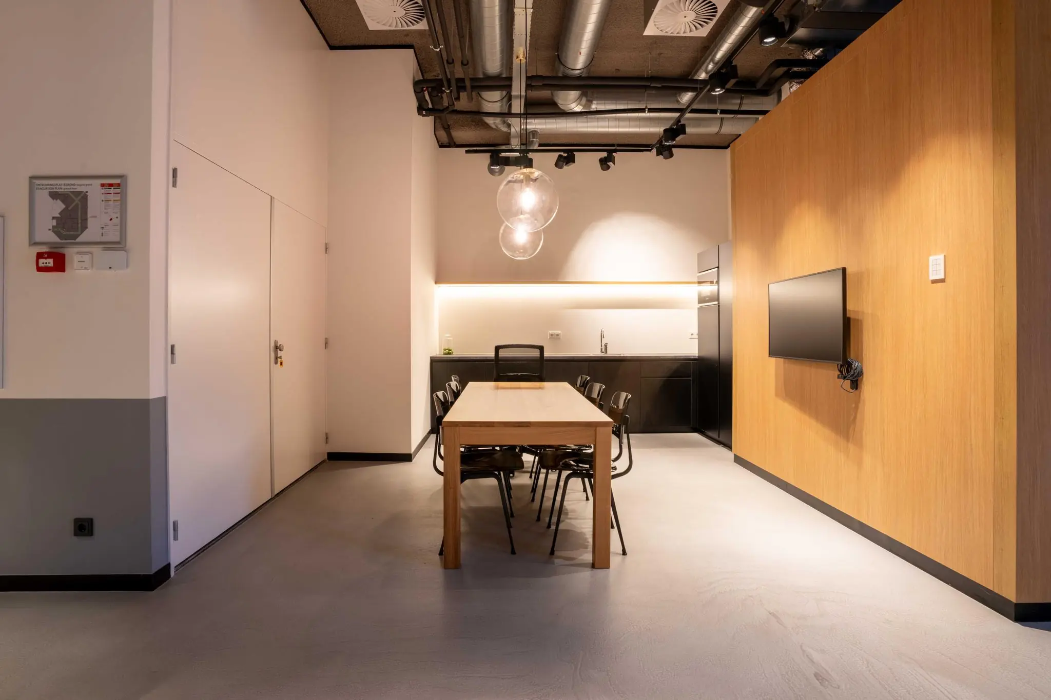 Moderne vergaderruimte met houten tafel, zwarte stoelen, kitchenette en wandtelevisie aan de 1e Hogeweg.